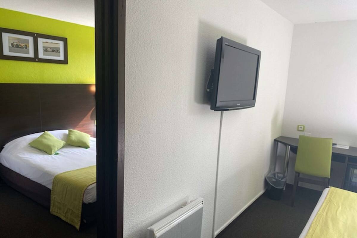 Ein Hotelzimmer mit Bett, Schreibtisch, Stuhl, Fernseher und Heizkörper.