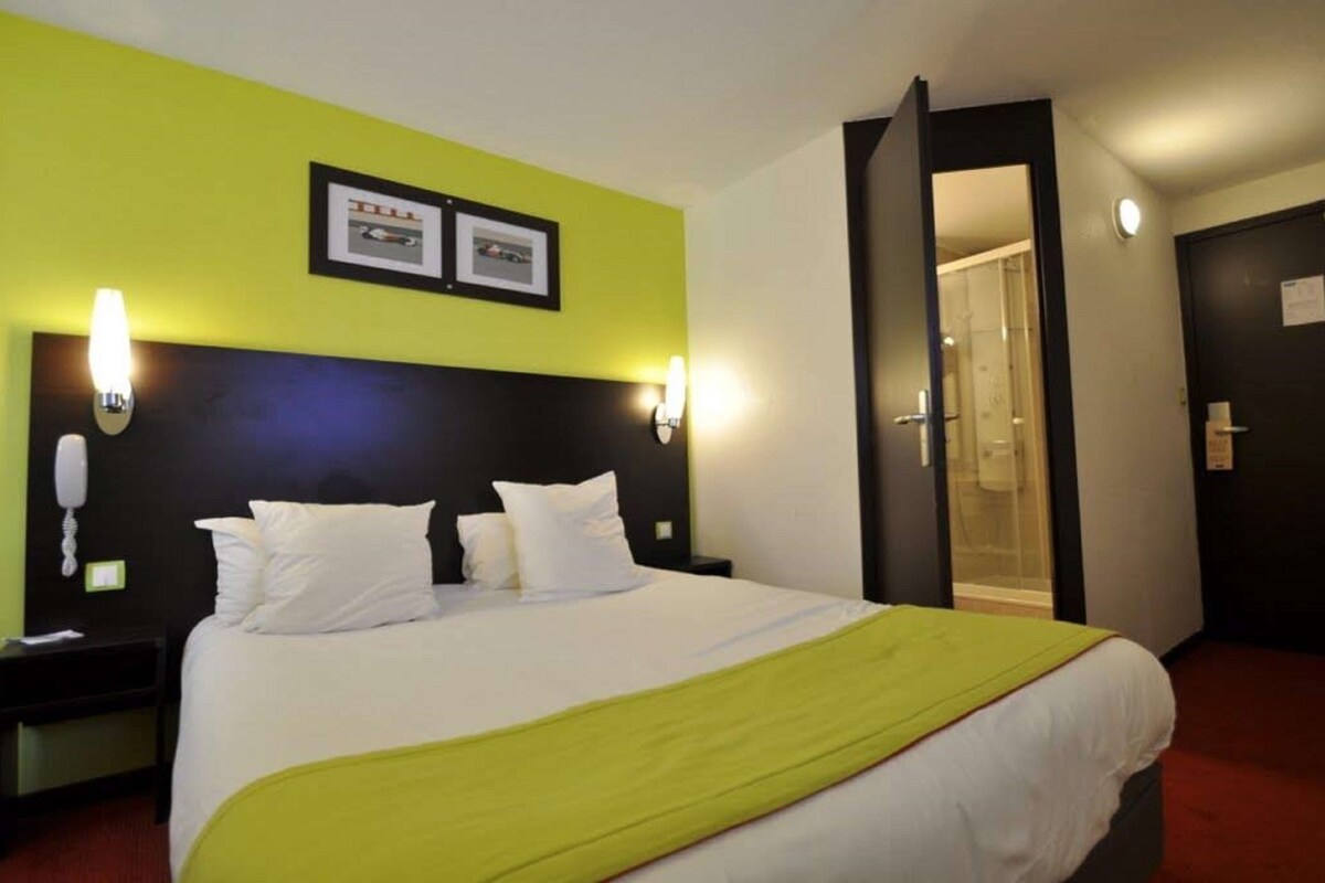 A hotel room with a bed, a phone on the nightstand, and a door leading to a bathroom.