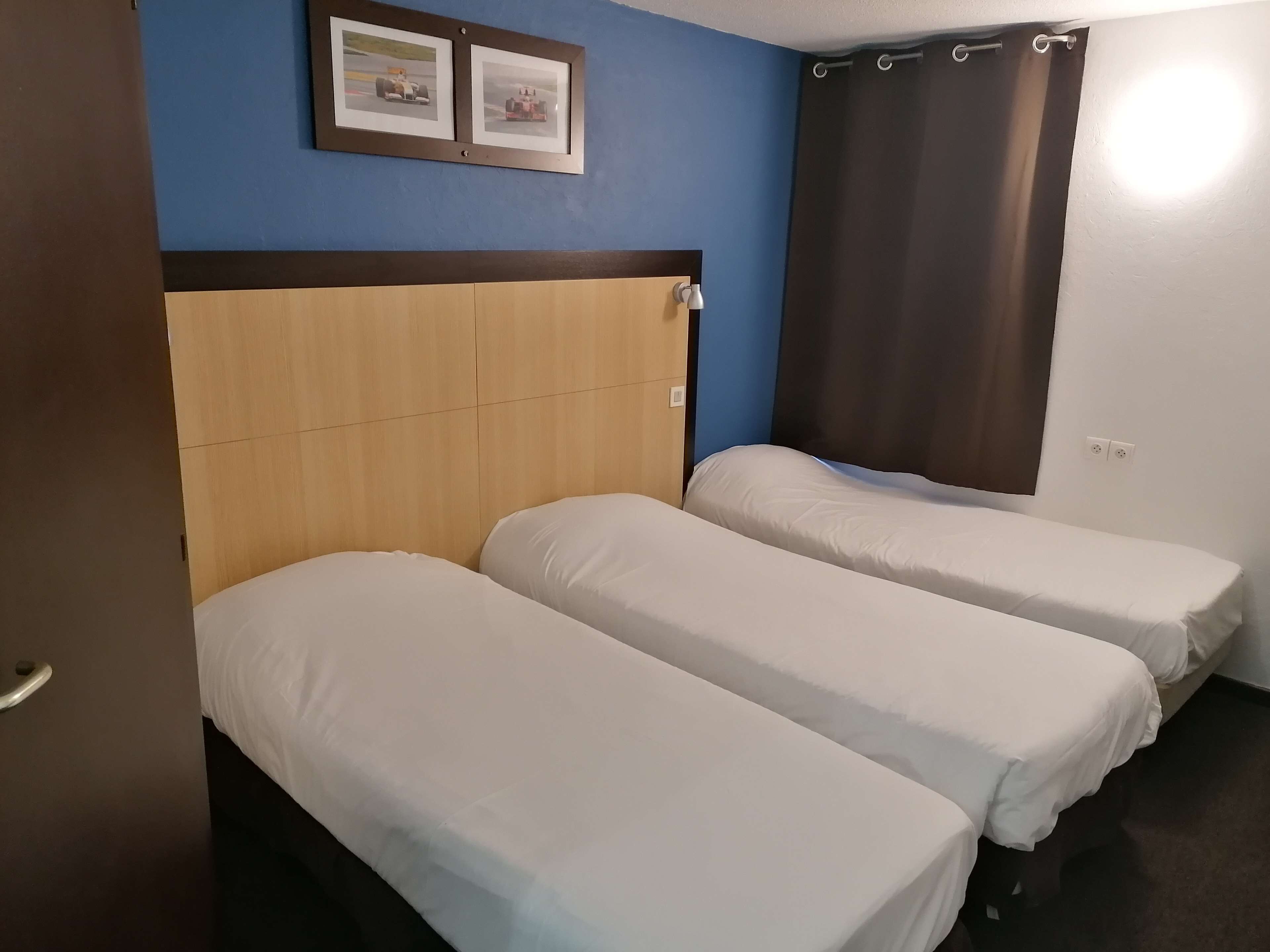 A hotel room with a wooden headboard, two single beds, a blue wall, and a framed picture above the beds.