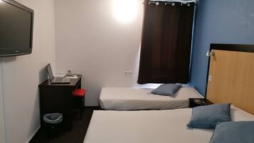 A hotel room with two beds, a desk with a laptop, a TV, and a window with curtains.