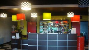 Zona de bar con suelo a cuadros, mostrador con diseño de rejilla y lámparas colgantes de colores.