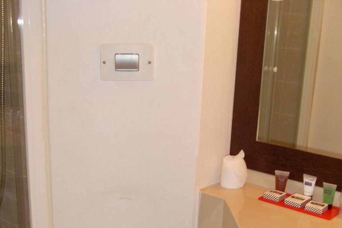 A small bathroom with a toilet, a sink, and a mirror. There is a shower curtain, a towel, and toiletries on the counter.