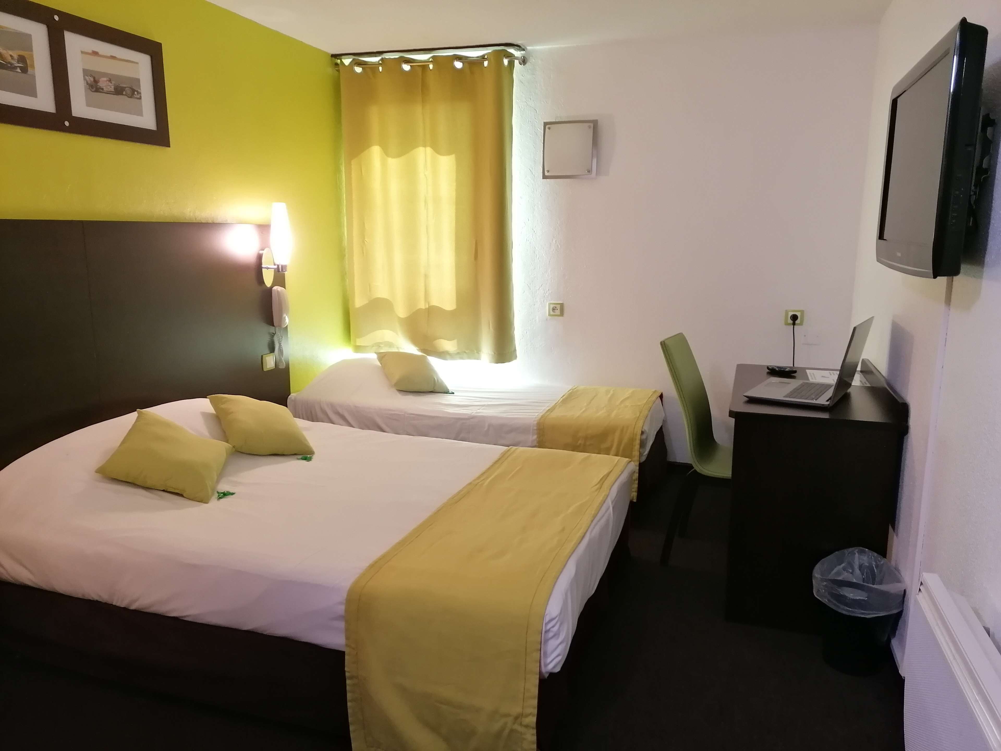 A hotel room with two beds, a desk with a laptop, a chair, and a TV on the wall.