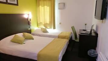 A hotel room with two beds, a desk with a laptop, a chair, and a TV on the wall.