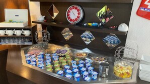 Un área de bufé con distintos alimentos, como yogur, frutas y un reloj en la pared.