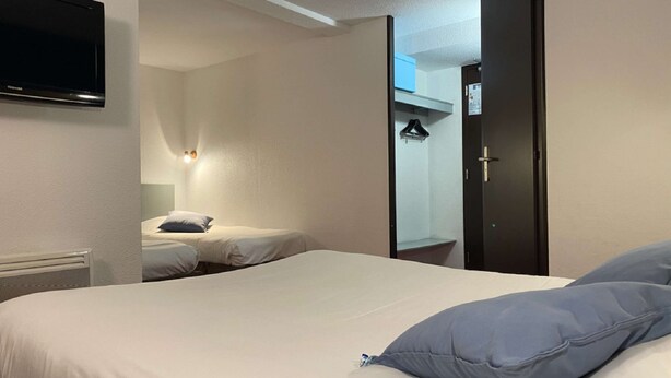 Una habitación de hotel con una cama, un televisor montado en la pared y una puerta que da a un baño.