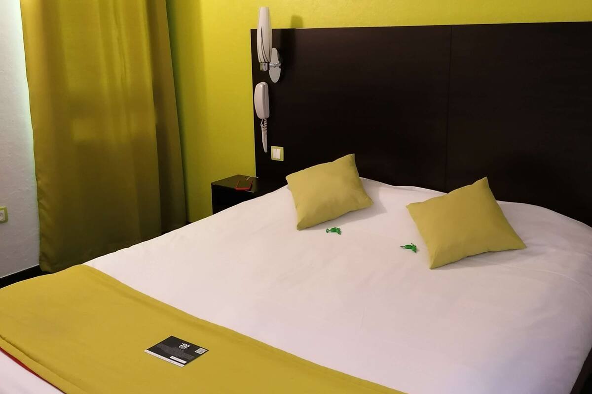 Ein Hotelzimmer mit einem Bett, einem Nachttisch, einem Telefon und zwei gerahmten Bildern an der Wand.