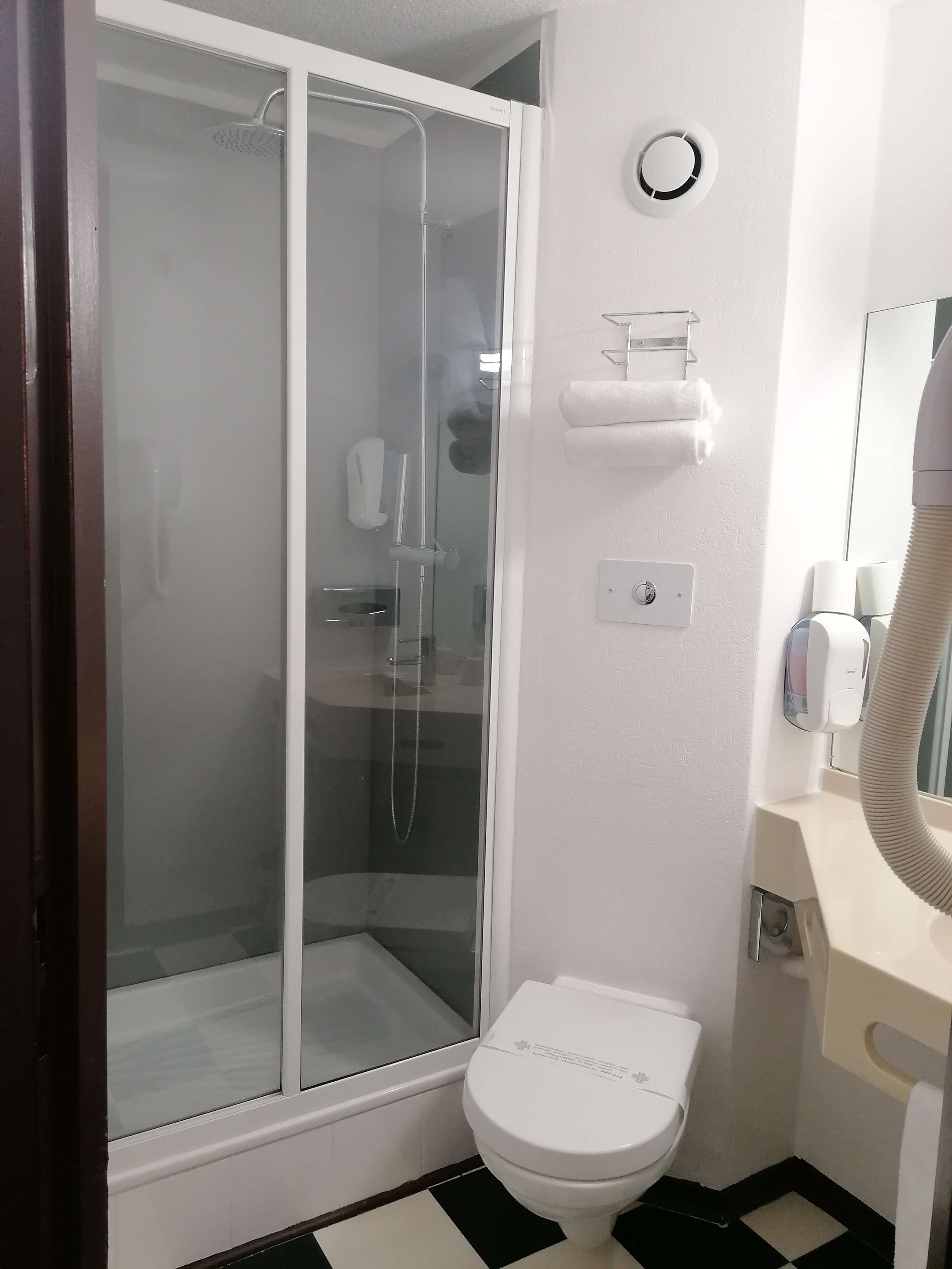 A bathroom with a glass-enclosed shower, a toilet, a towel dispenser, and a hand dryer.