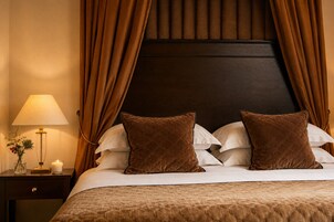 Una cama bien hecha con almohadas marrones, una mesita de noche con una lámpara y una vela, y un cabecero oscuro.