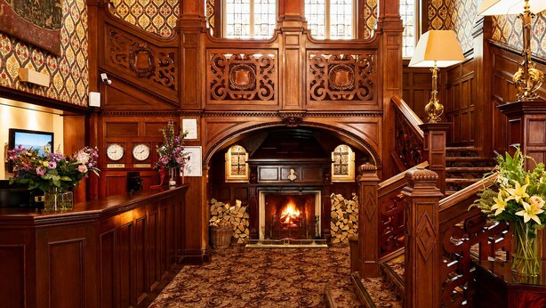 A grand lobby with a fireplace, wooden paneling, and a staircase. - Macdonald Frimley Hall Hotel and Spa (Camberley)