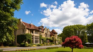 A large, historic building with multiple wings and a prominent tower, surrounded by well-maintained lawns and trees. - Macdonald Frimley Hall Hotel and Spa (Camberley)