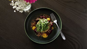 Een donker houten tafel met een groen bord waarop een gerecht, een vork en een vaas met bloemen staan.