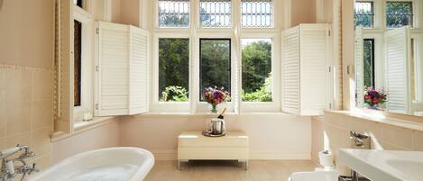 Un baño con bañera, tocador, ventana con contraventanas y espejo.