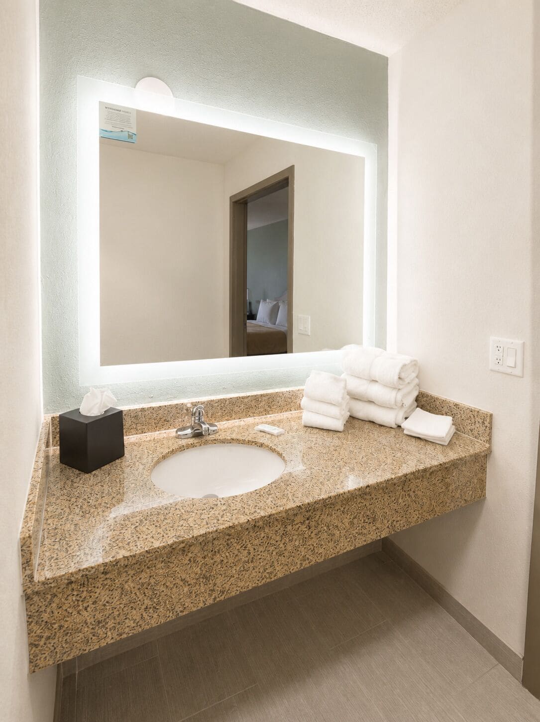Ein Badezimmer mit einem Waschbecken aus Granit, einem Spiegel und einem Stapel weißer Handtücher.