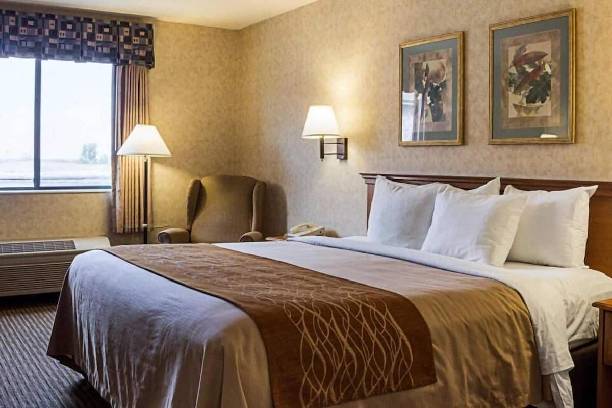 A hotel room with a bed, two wall-mounted lamps, a chair, and two framed pictures on the wall.