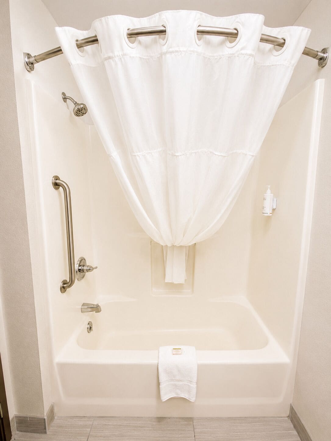 A standard white bathtub with a shower curtain, grab bars, and a handheld showerhead.