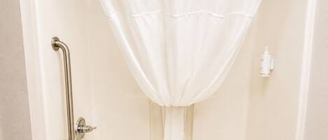 A standard white bathtub with a shower curtain, grab bars, and a handheld showerhead.