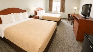 A hotel room with two beds, a desk with a TV, a chair, a desk lamp, and a window with curtains.
