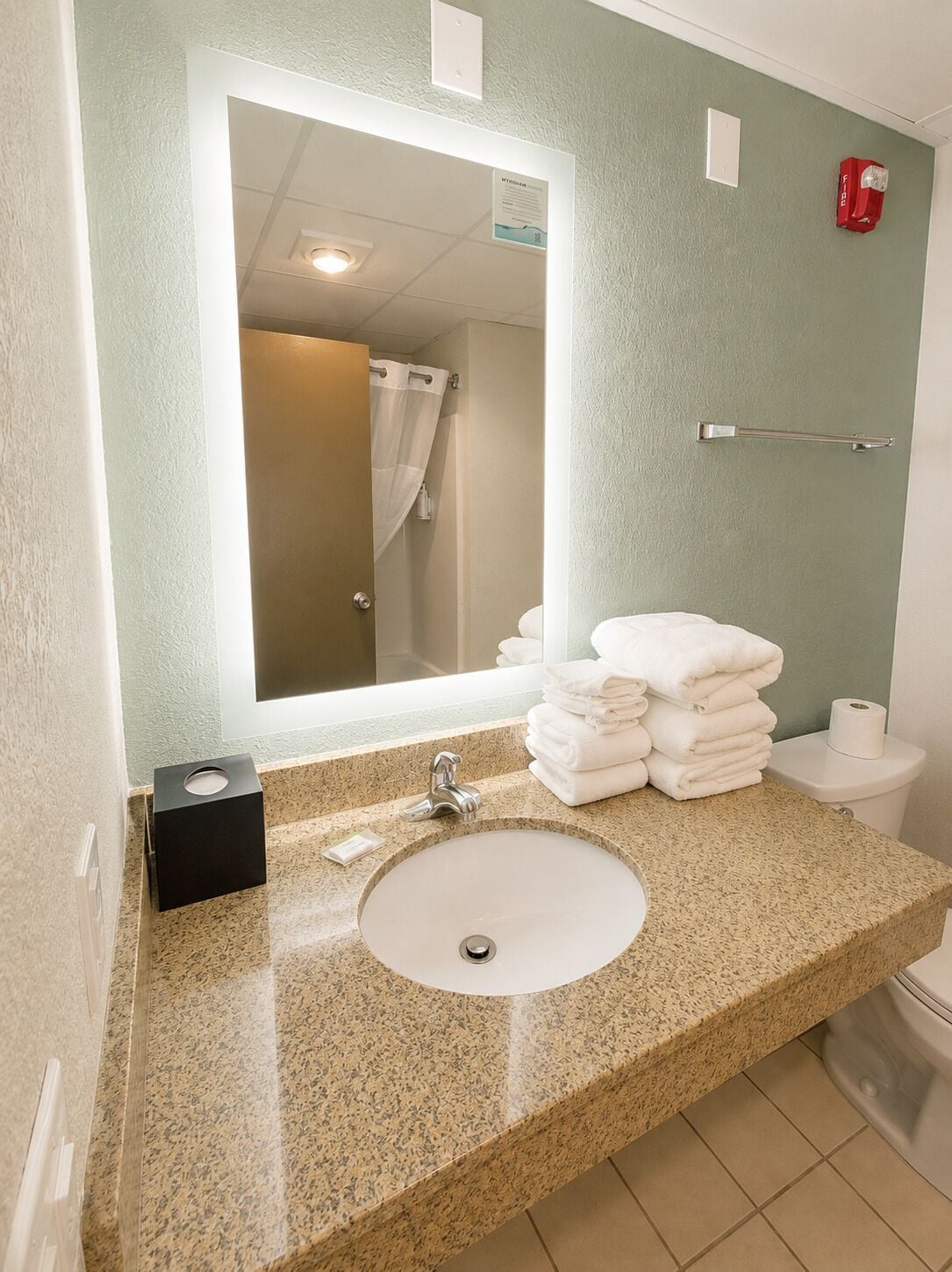 A bathroom with a granite countertop, a sink, a mirror, a towel rack, and a toilet.