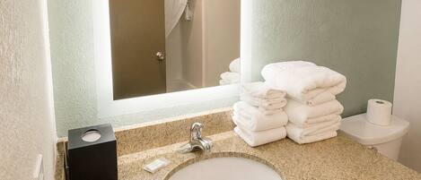 A bathroom with a granite countertop, a sink, a mirror, a towel rack, and a toilet.