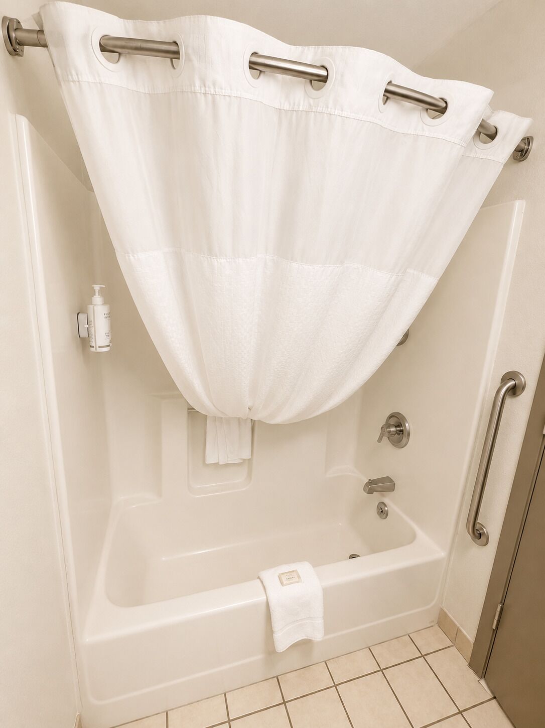 A bathroom with a bathtub, a shower curtain, a towel, and a handrail.