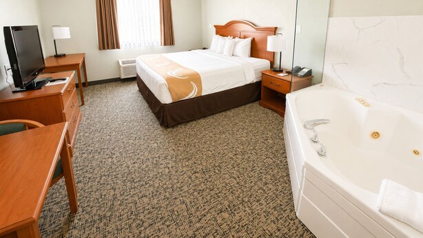 A hotel room with a bed, a desk, a television, a desk lamp, a telephone, and a bathtub. - Travelodge by Wyndham Rapid City/Black Hills (Rapid City)
