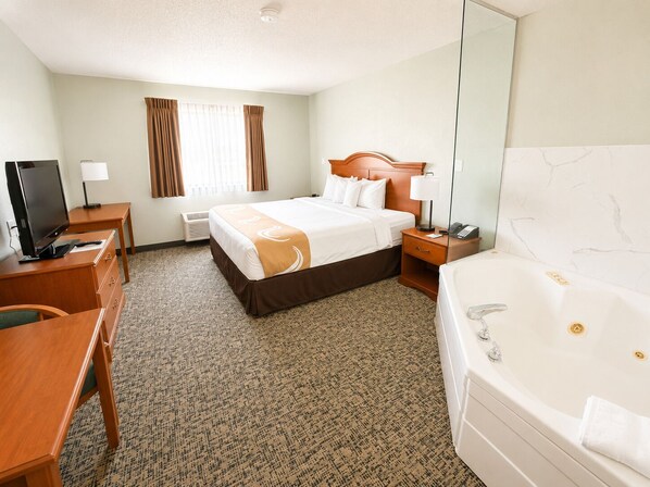 A hotel room with a bed, a desk, a television, a desk lamp, a telephone, and a bathtub.