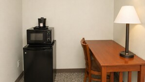 A small kitchenette with a microwave and a refrigerator, a wooden dining table with a chair, and a floor lamp. - Travelodge by Wyndham Rapid City/Black Hills (Rapid City)