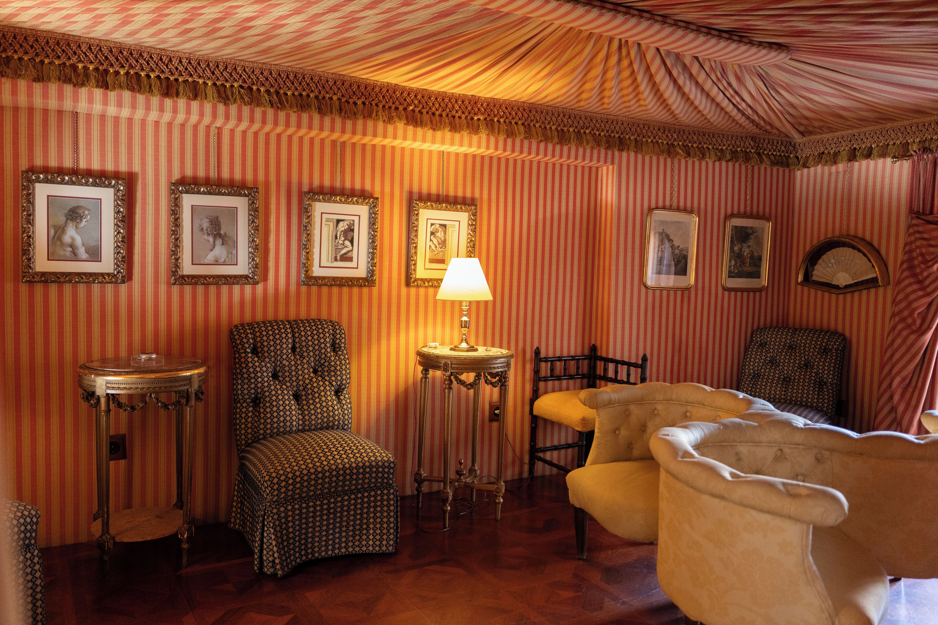 A room with striped wallpaper, a lamp, and several chairs.