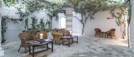 An outdoor patio with wicker furniture, stone flooring, and a pergola covered in vines.