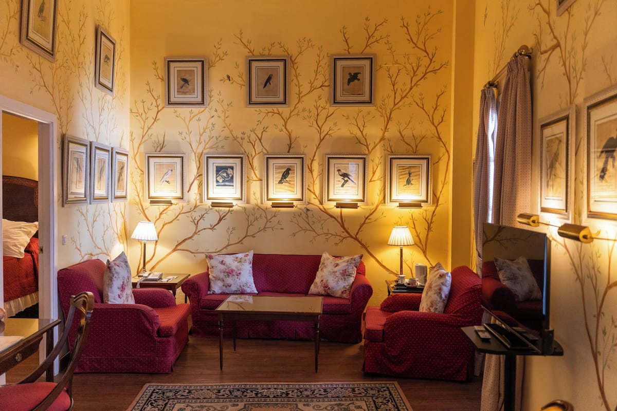 A cozy living room with a red sofa set, a coffee table, and a TV. There are framed pictures on the wall and a lamp on the side table.