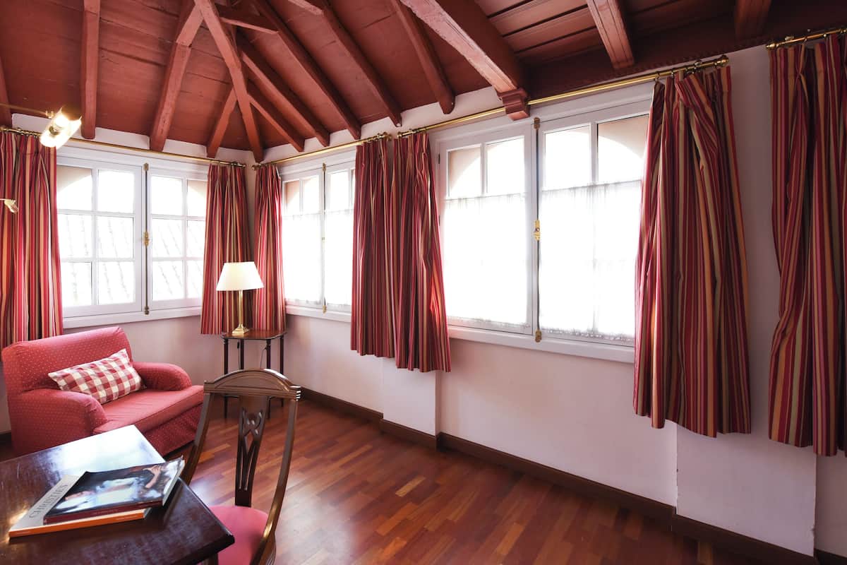 A room with wooden flooring, a red sofa, a table with a magazine, and striped curtains on the windows.