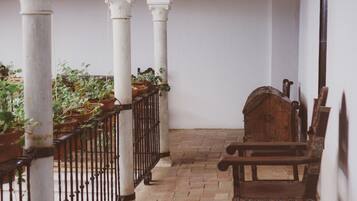 Un espacio al aire libre techado con un banco de madera, plantas en macetas y piso de baldosas.