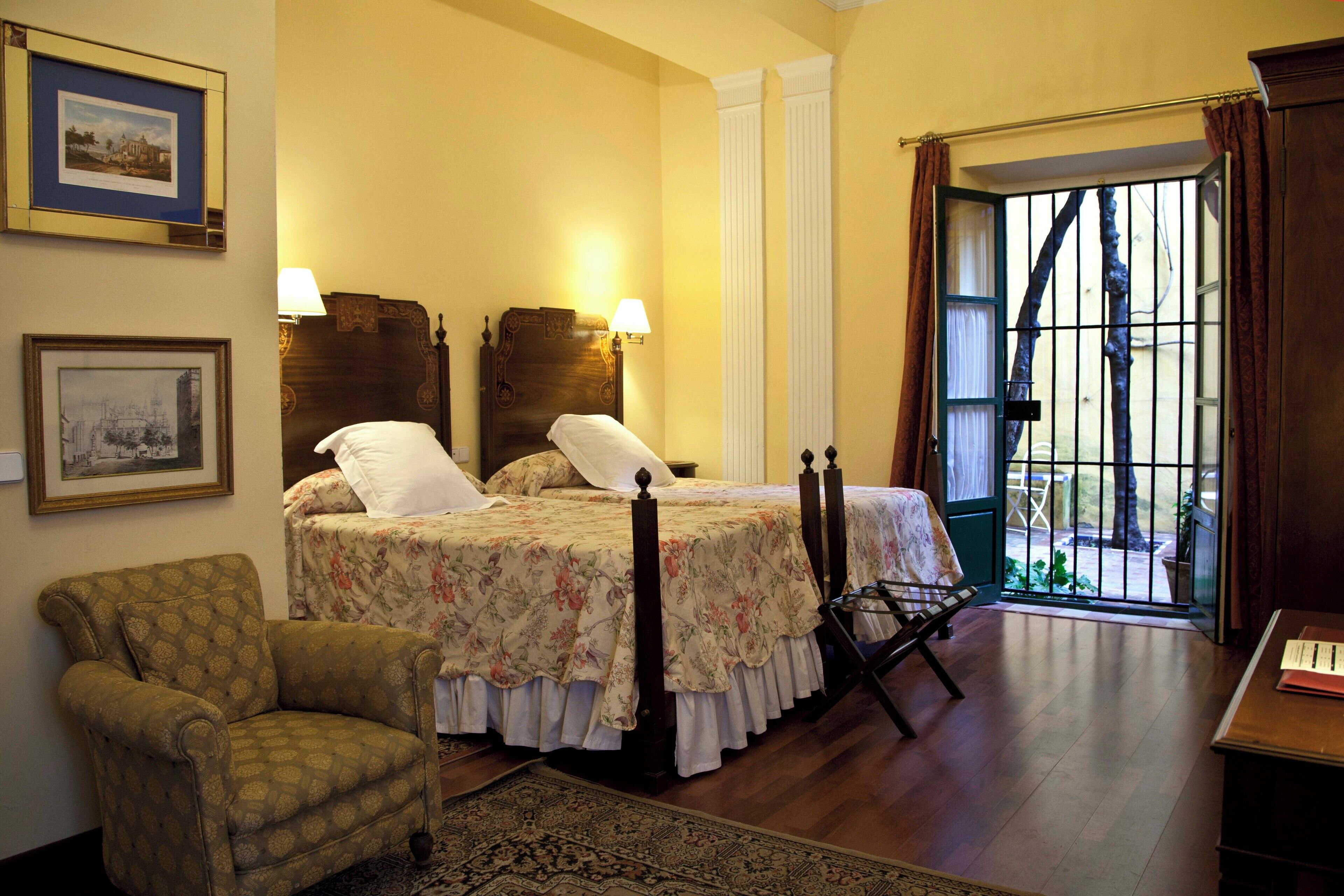 Un dormitorio con cama, una silla, un escritorio y una ventana con cortinas.