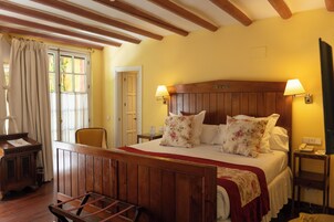 Una habitación con una cama de madera, dos lámparas de noche, una mesita de noche de madera, una silla y un ventanal con cortinas.
