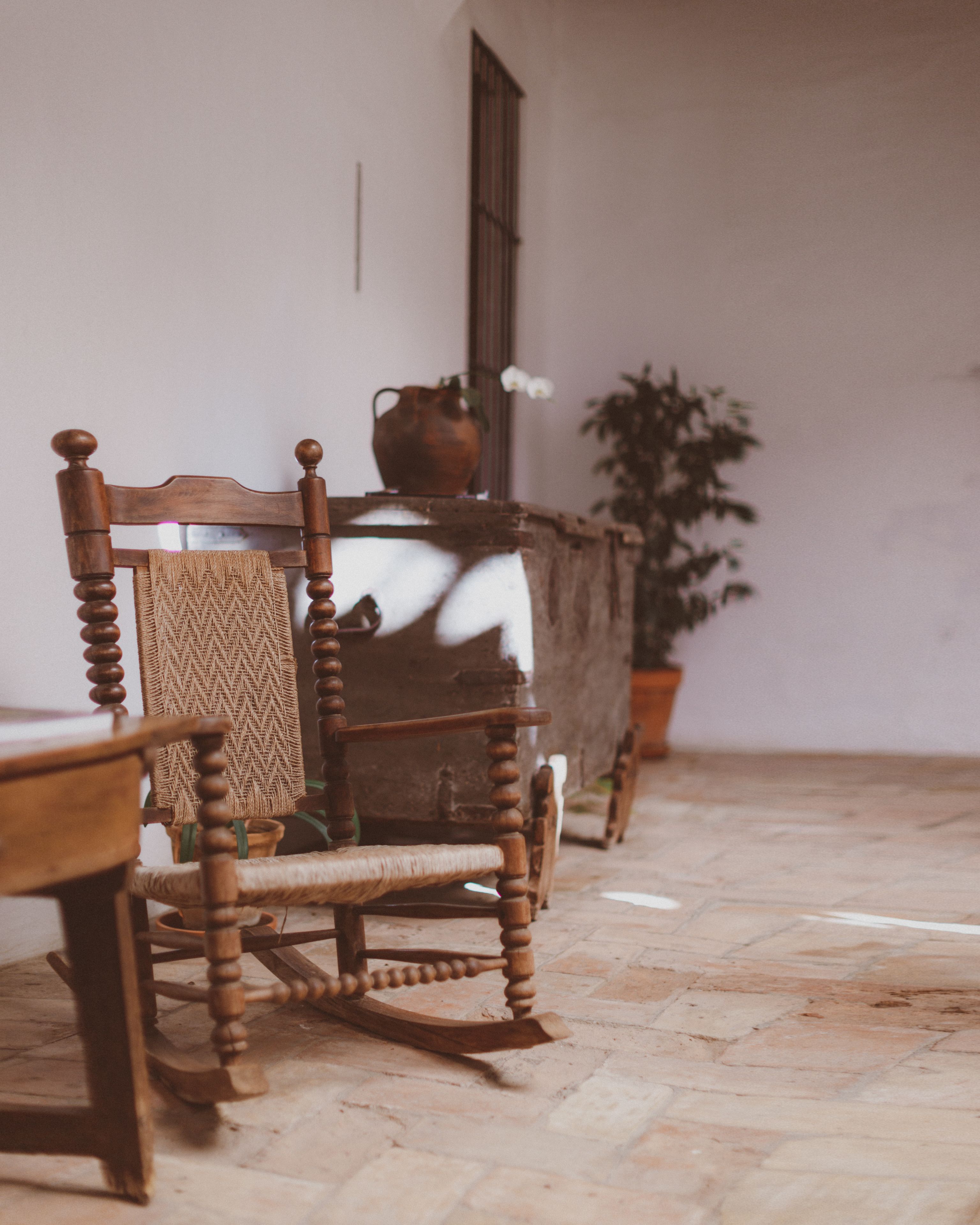 A rustic wooden chair with a woven seat and backrest, positioned next to a table with a vase and a potted plant.