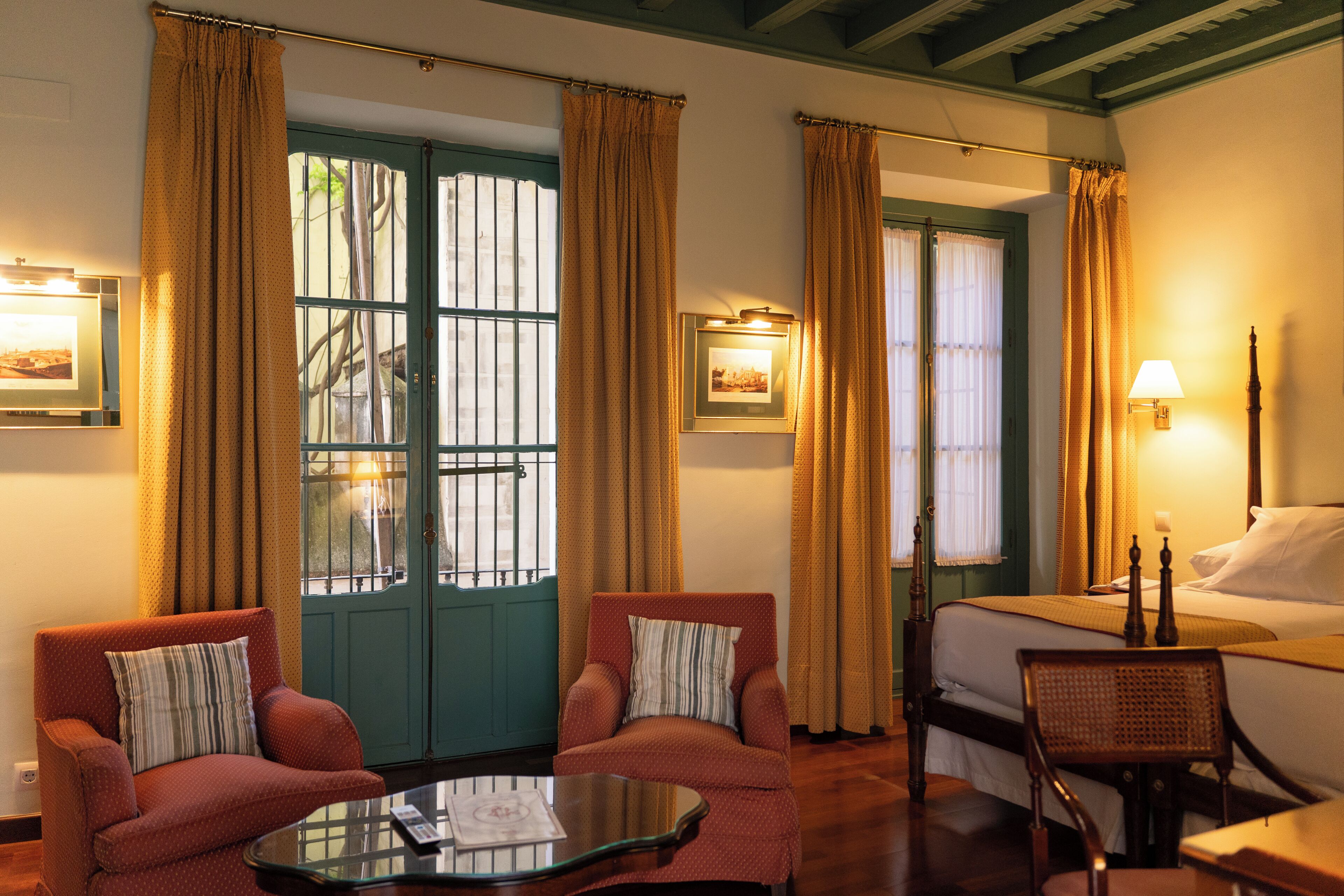 A hotel room with two armchairs, a bed, a nightstand, and a window with curtains.