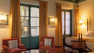 A hotel room with two armchairs, a bed, a nightstand, and a window with curtains.