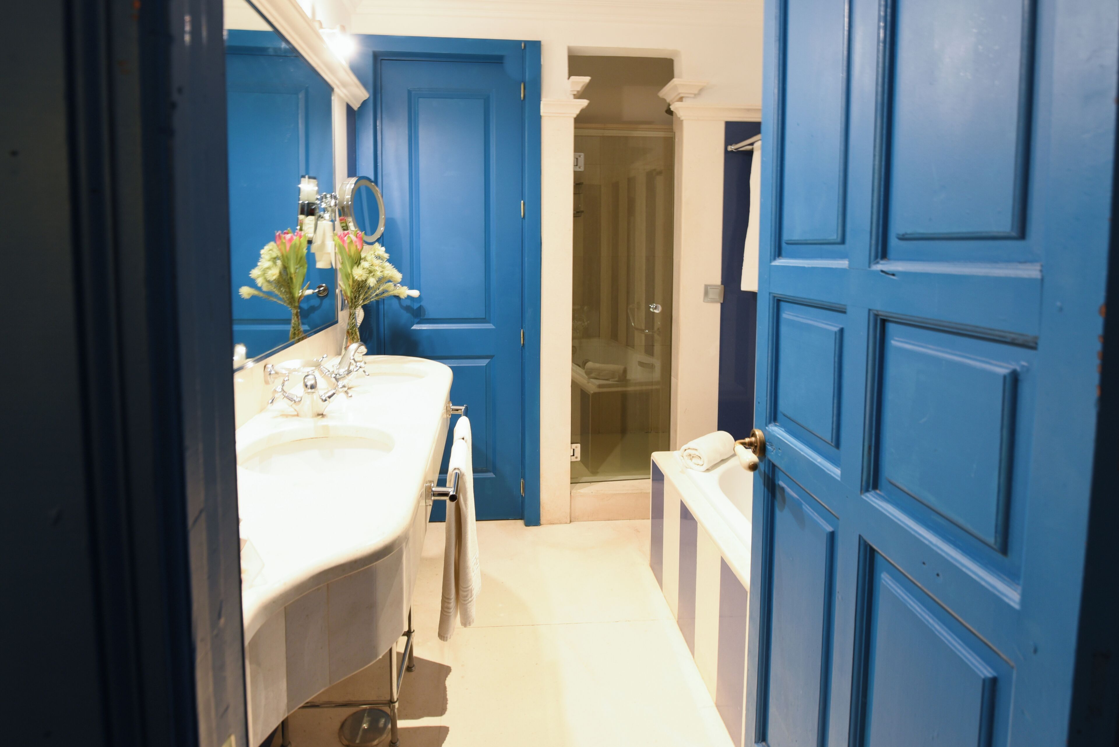 Une salle de bain avec un lavabo blanc, un miroir et une porte bleue.