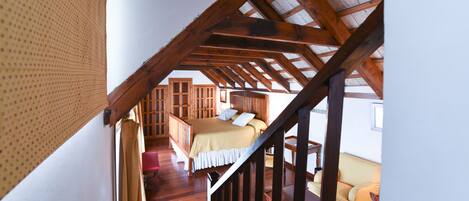 A bedroom with a wooden ceiling, a bed with a white and beige bedspread, and a wooden dresser.