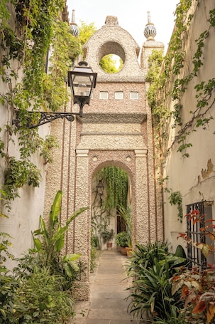 A narrow alleyway with a stone archway, potted plants, and a hanging lantern.