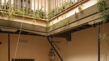 Un patio con suelo a cuadros, mobiliario de madera, plantas en macetas y un balcón con barandillas.