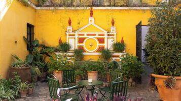 A courtyard with yellow walls, a decorative gate, potted plants, and green chairs.