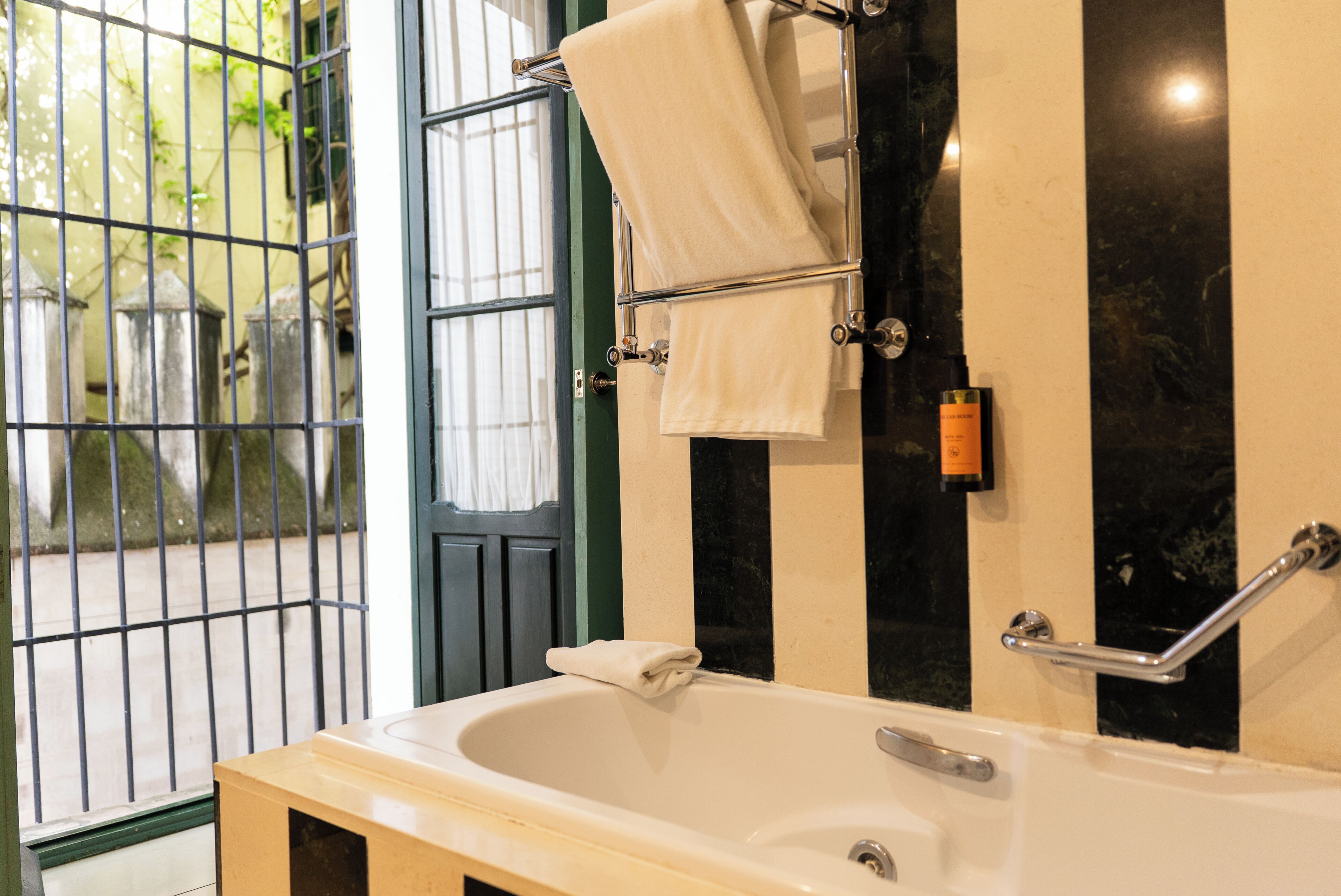 A bathroom with a bathtub, a towel rack, a handrail, and a door with a metal gate.