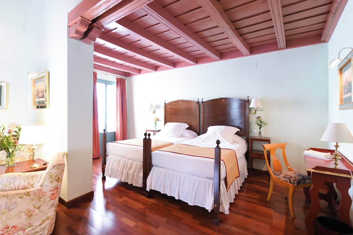A bedroom with a large bed, wooden headboard, and a wooden ceiling. There is a chair and a table with a lamp.