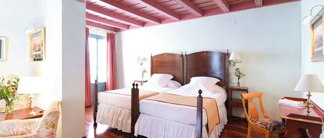 A bedroom with a large bed, wooden headboard, and a wooden ceiling. There is a chair and a table with a lamp.