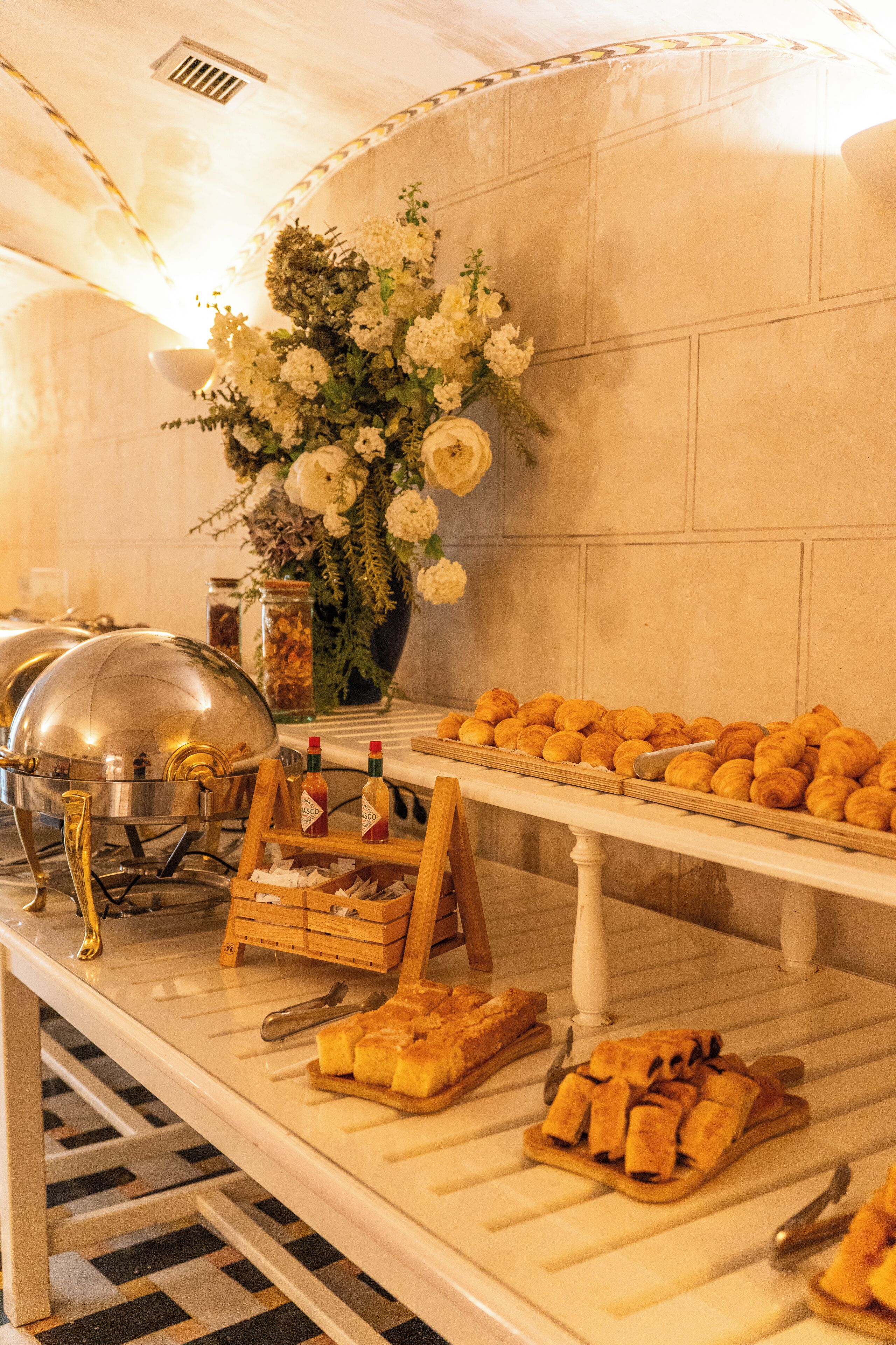 A buffet setup with various food items, a flower arrangement, and a buffet station with a metal dome cover.. Las Casas de la Judería, Sevilla Historic City Center