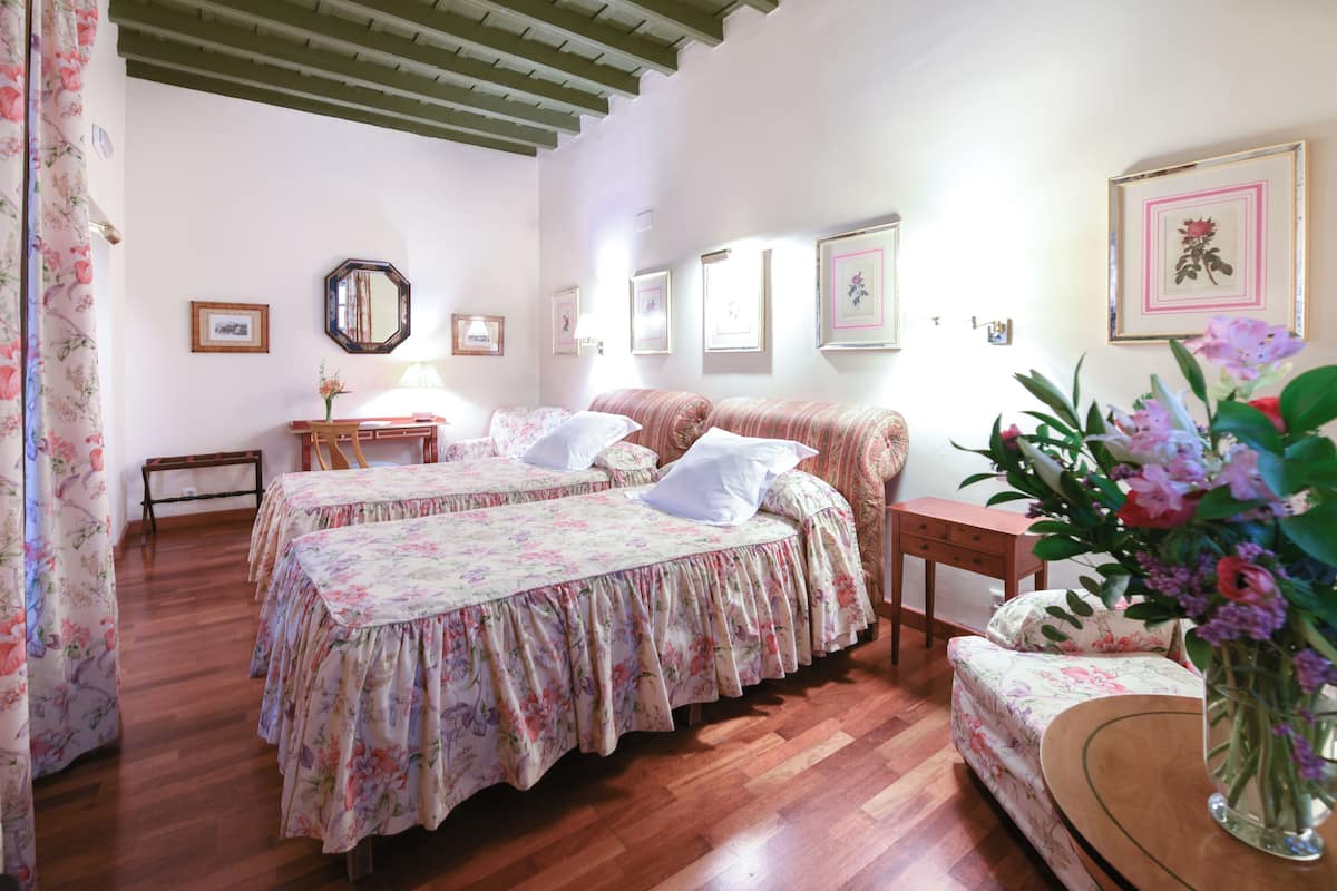 A bedroom with two beds, a wooden bench, a small table, and a mirror.