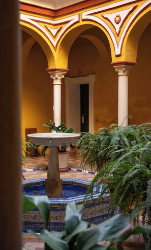 Une cour avec une fontaine, des arcades, des colonnes et des plantes en pot.