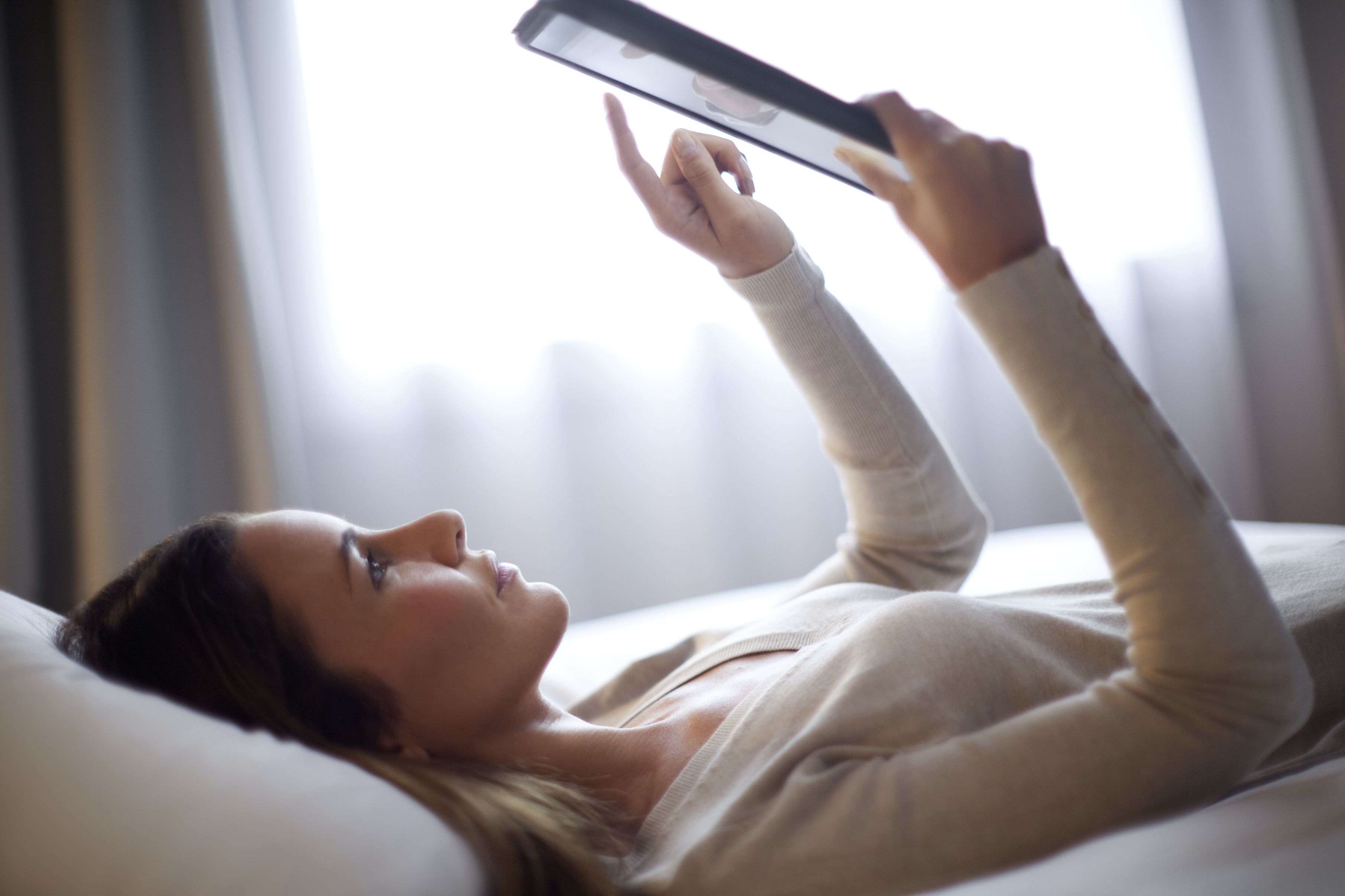 A person lying on a bed with a tablet in hand.